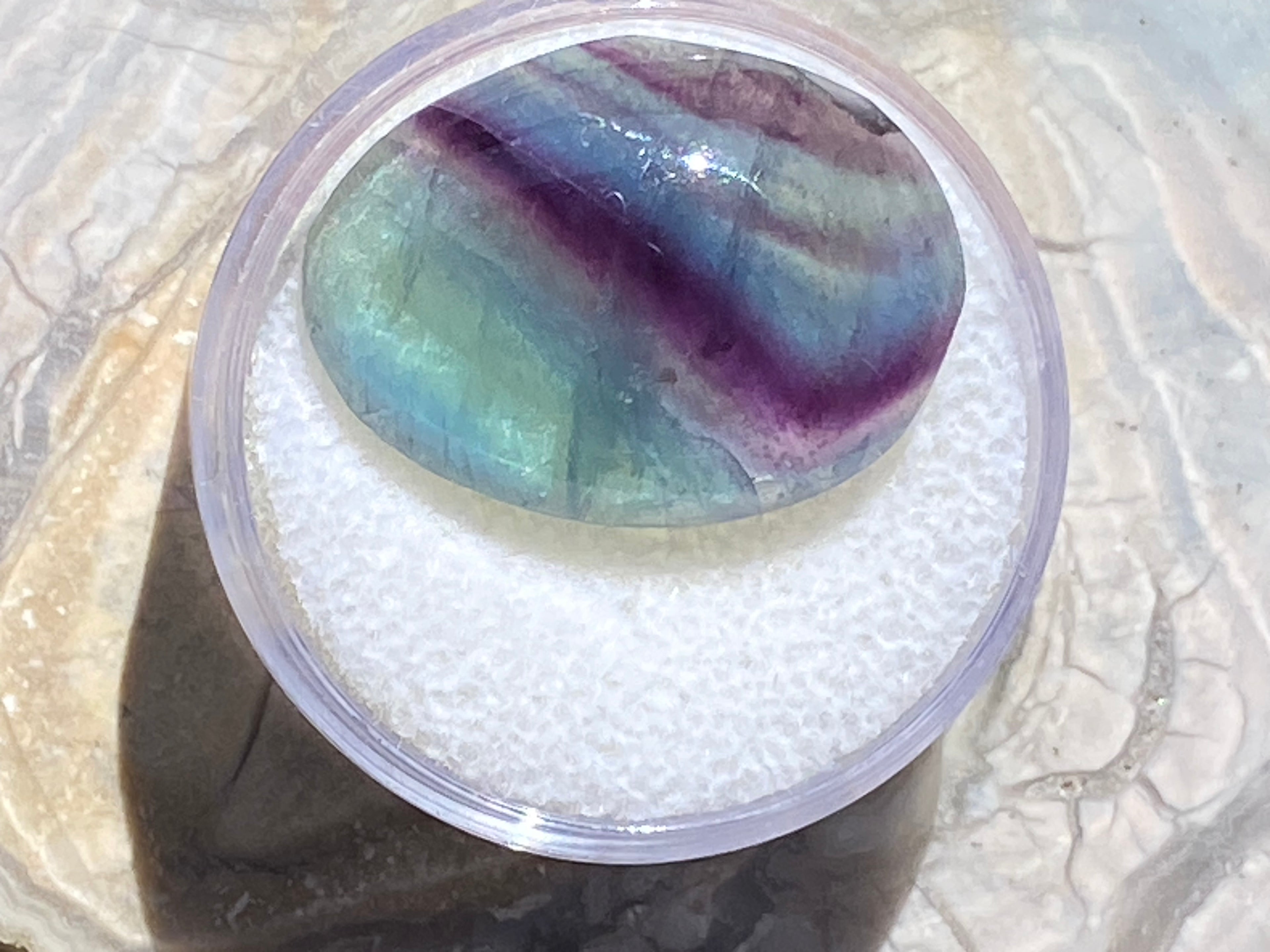Multicolored stone in a clear container on a textured surface