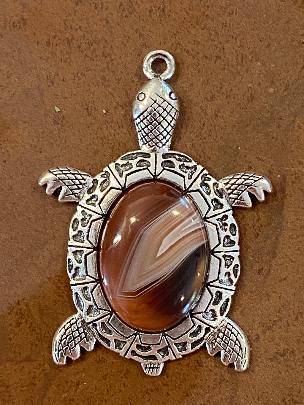 Tortoise-shaped pendant with a brown gemstone on a brown background