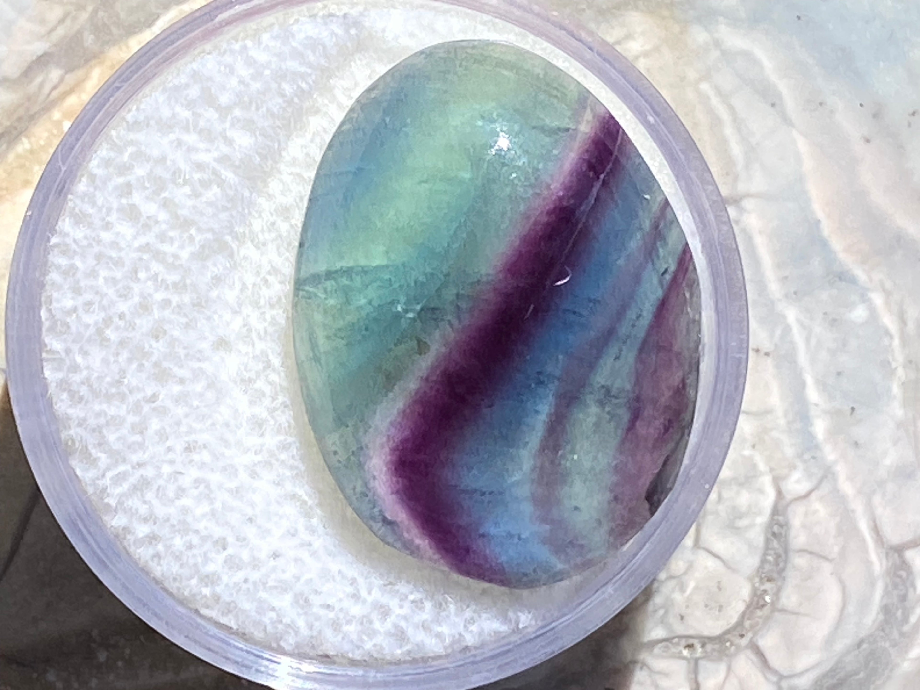 Multicolored stone in a clear container on a textured surface