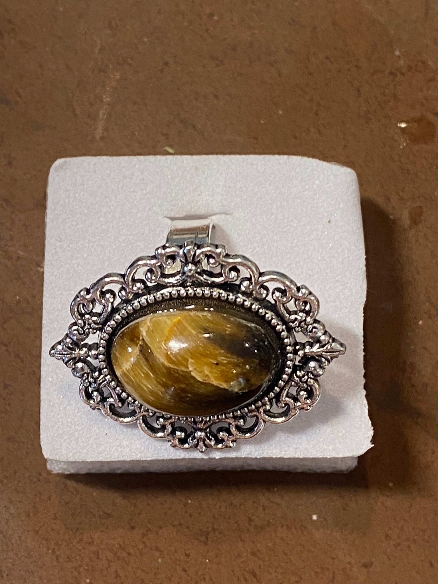 Silver pendant with a yellow stone on a white stand against a brown background