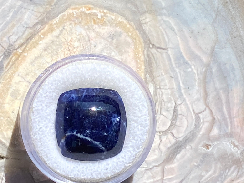 Blue gemstone in a clear plastic holder on a textured white background