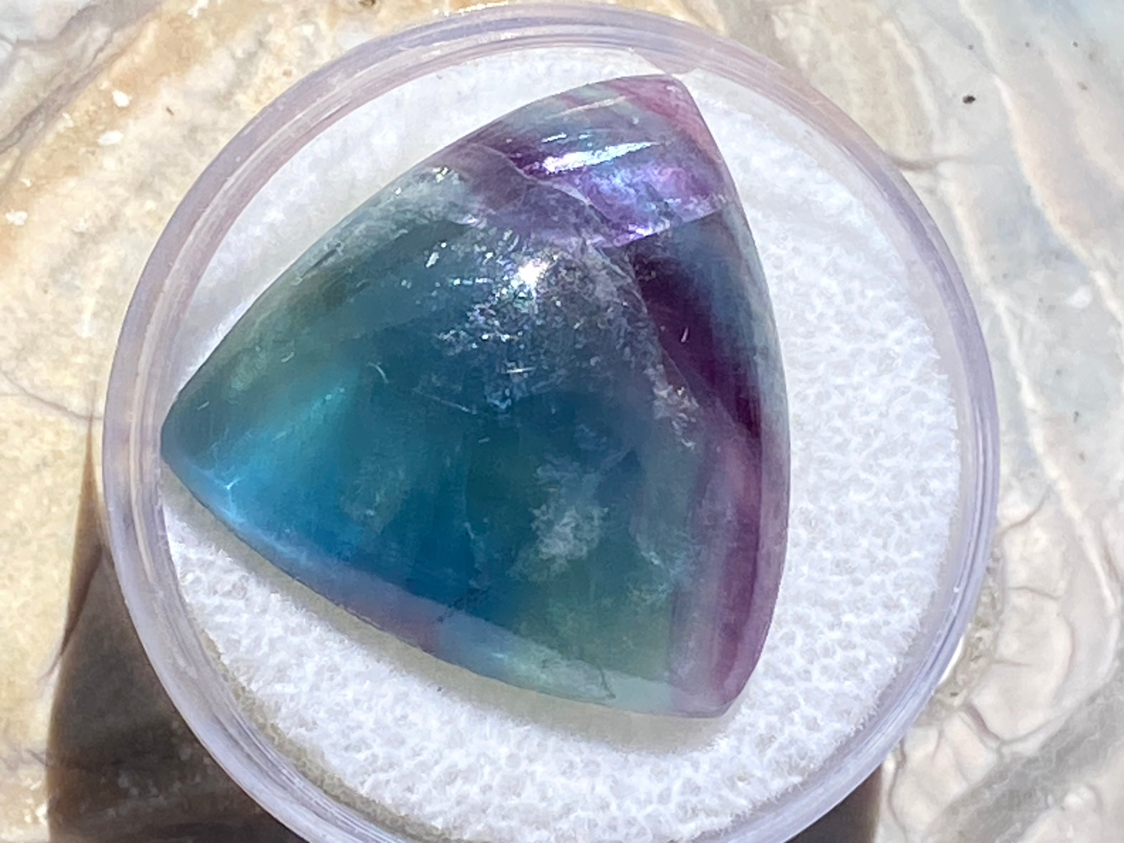 Multicolored gemstone in a clear container on a textured surface