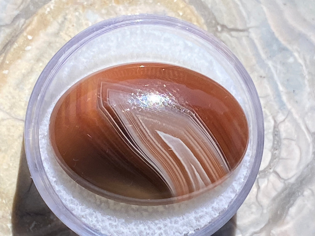 Close-up of a container with a brown and white agate on a textured surface