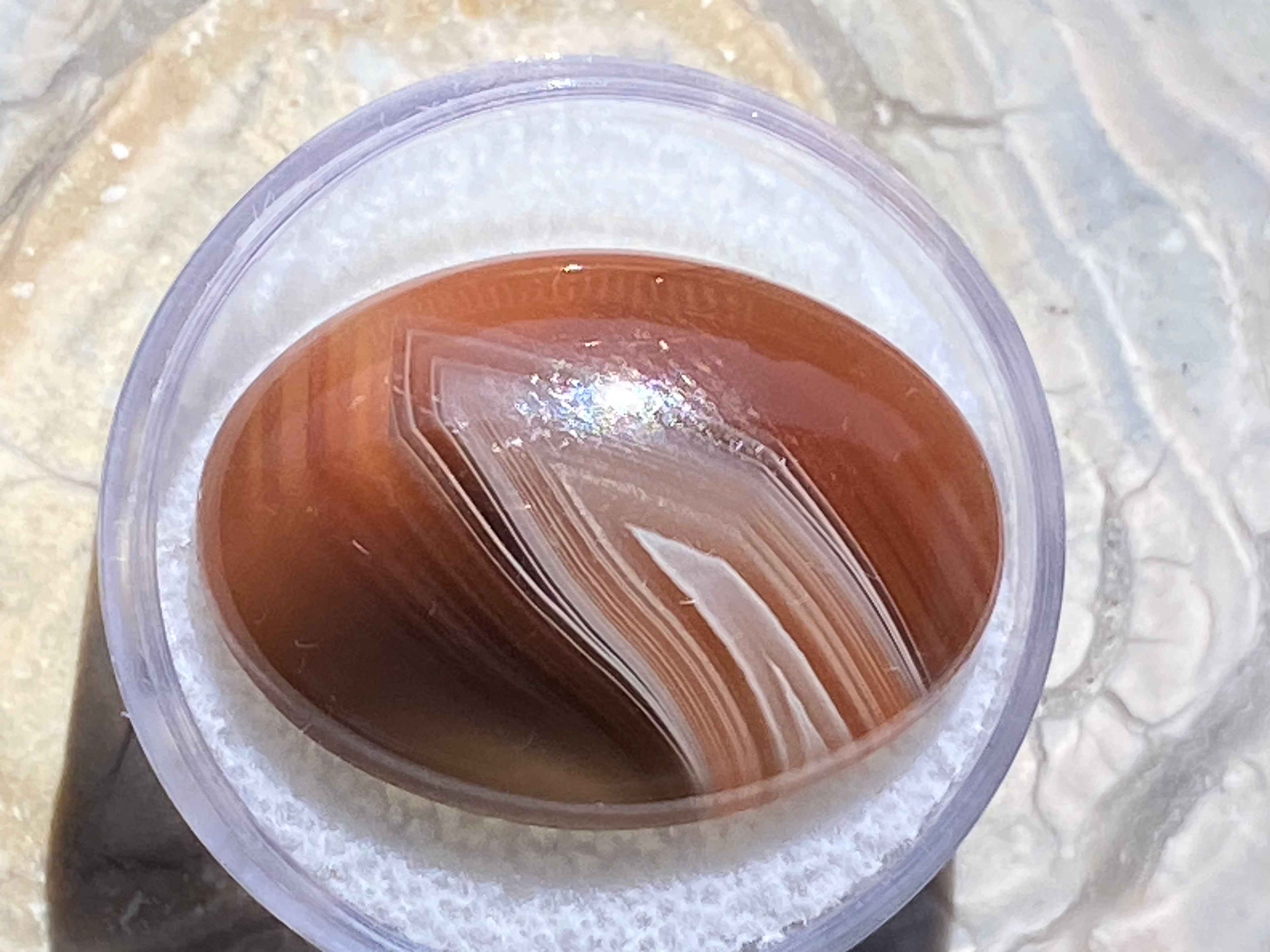 Close-up of a container with a brown and white agate on a textured surface