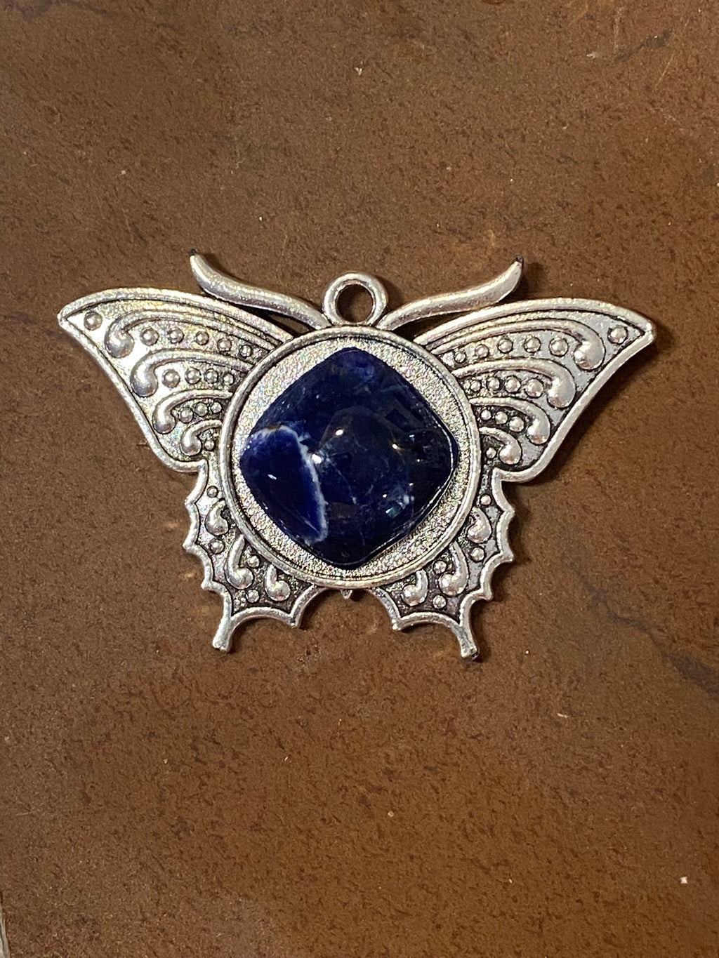 Butterfly-shaped pendant with blue stone on a brown background