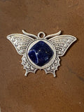 Butterfly-shaped pendant with blue stone on a brown background