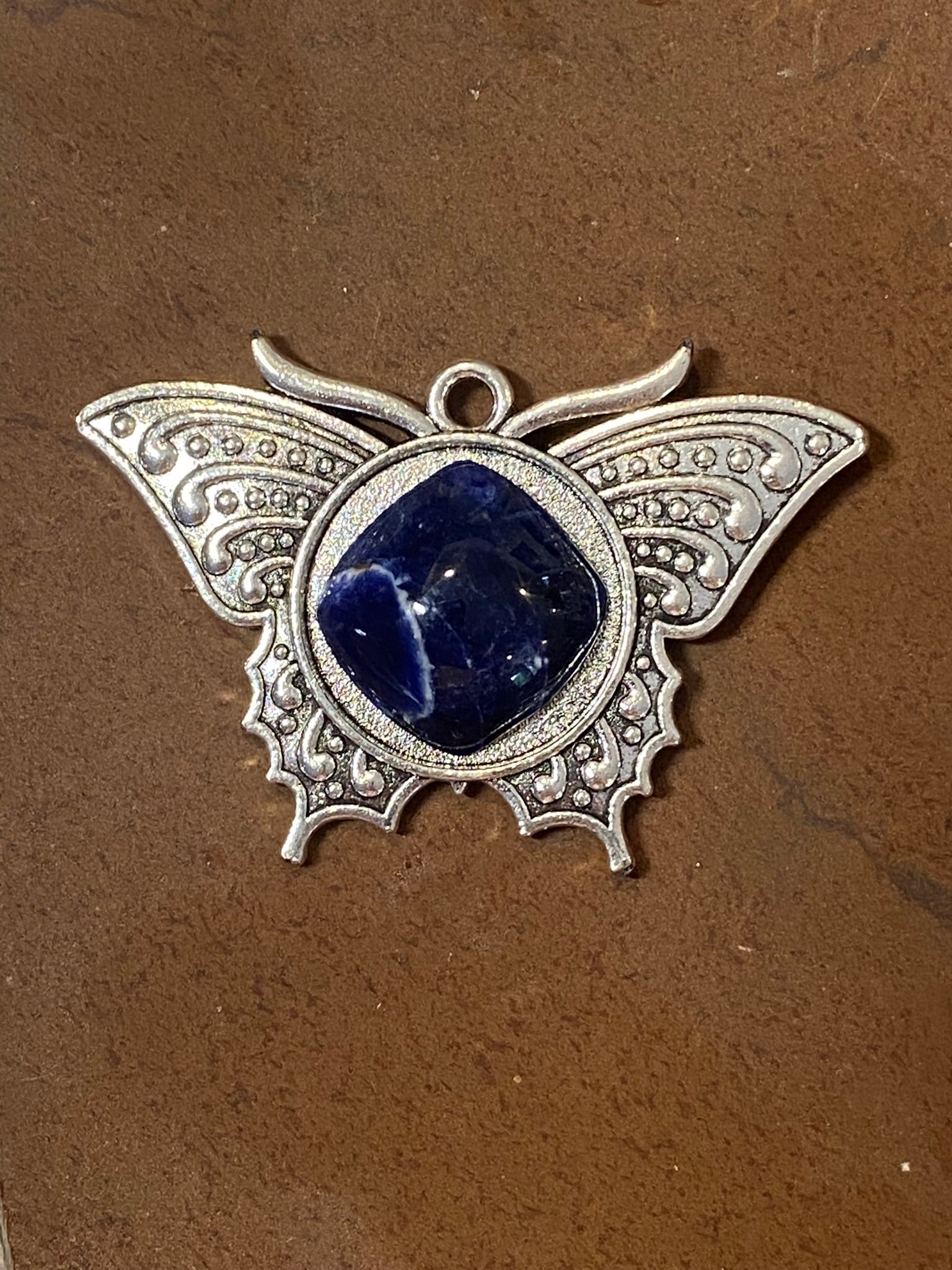Butterfly-shaped pendant with blue stone on a brown background