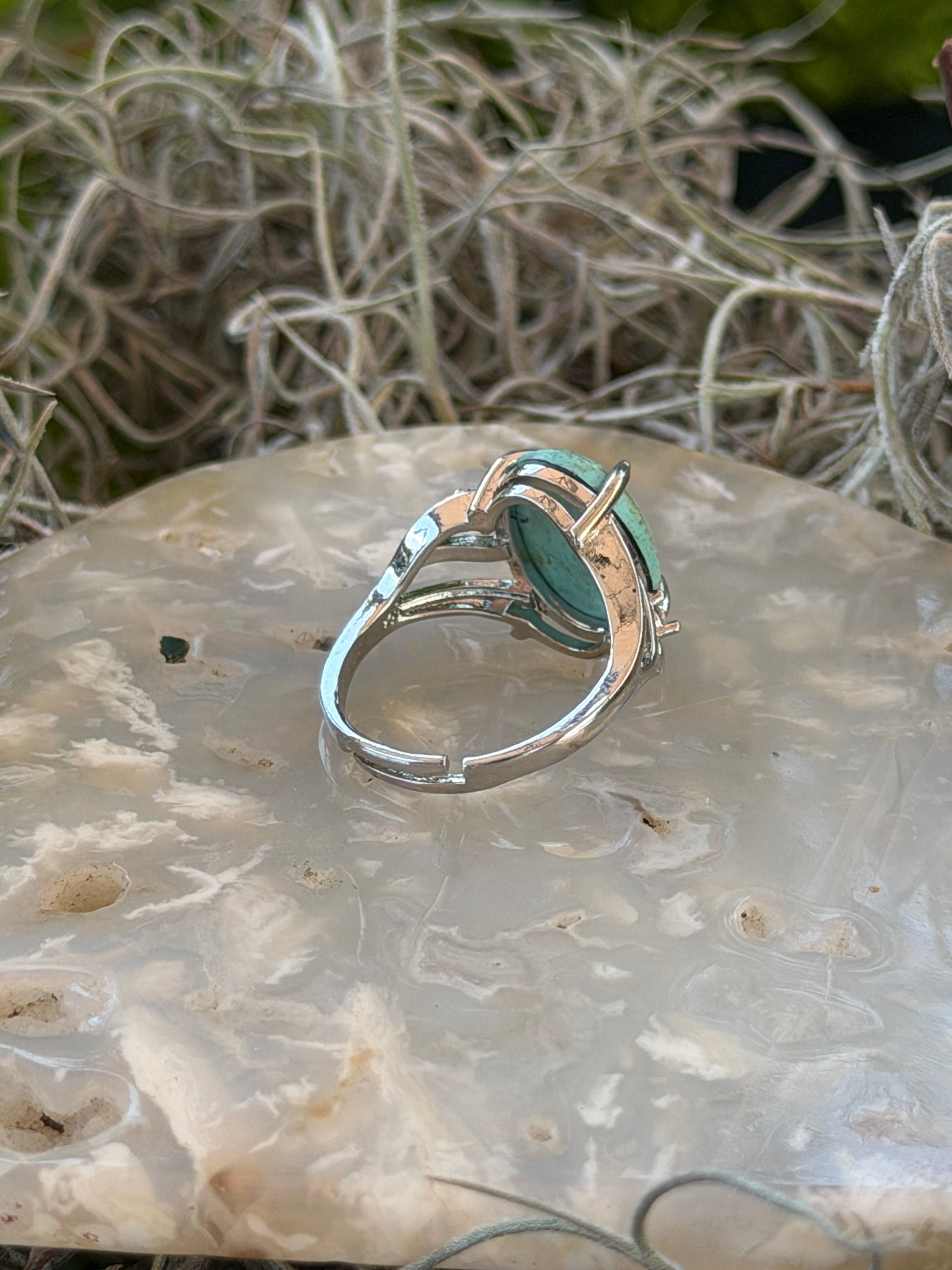 A silver ring with a green stone, displayed on a textured white agate slab next to dried Spanish moss.