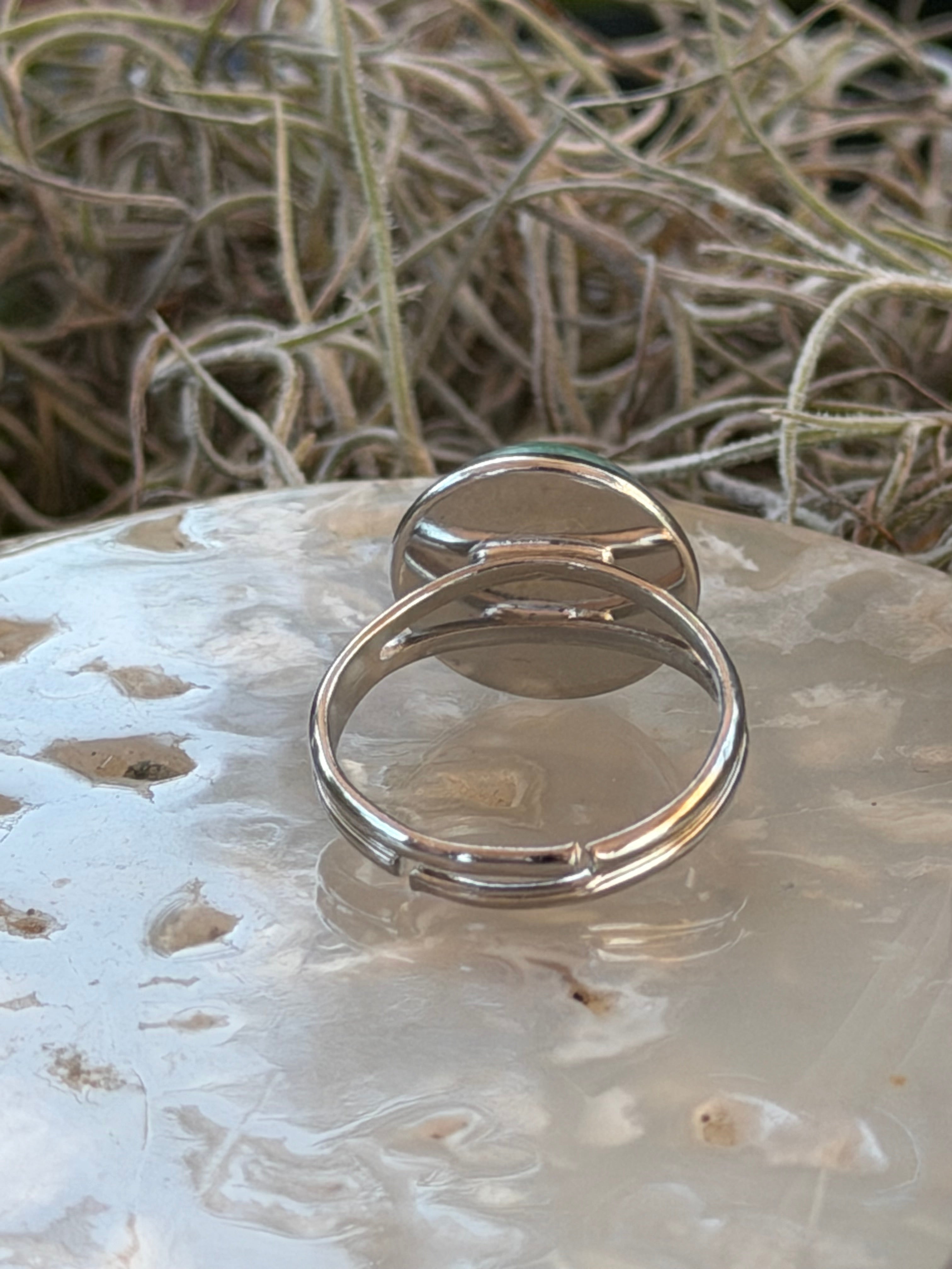 Two polished silver-toned metal rings with a unique side-tab design, displayed on a textured white stone surface next to dried grass.