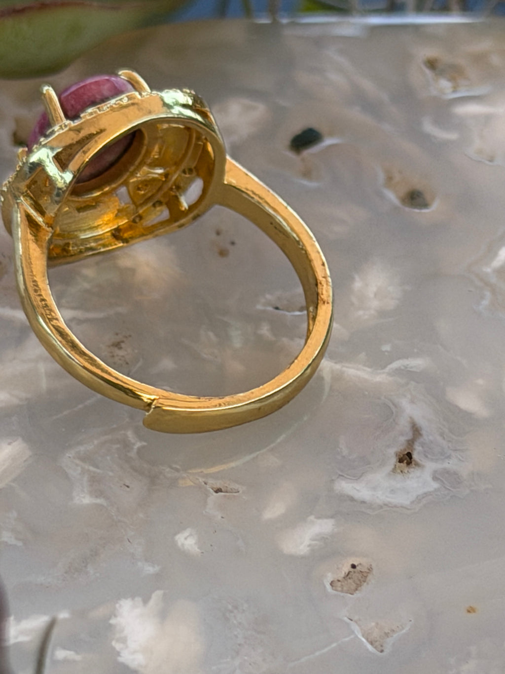 A gold ring with a large oval pink gemstone, shown close-up on a textured, translucent white surface.