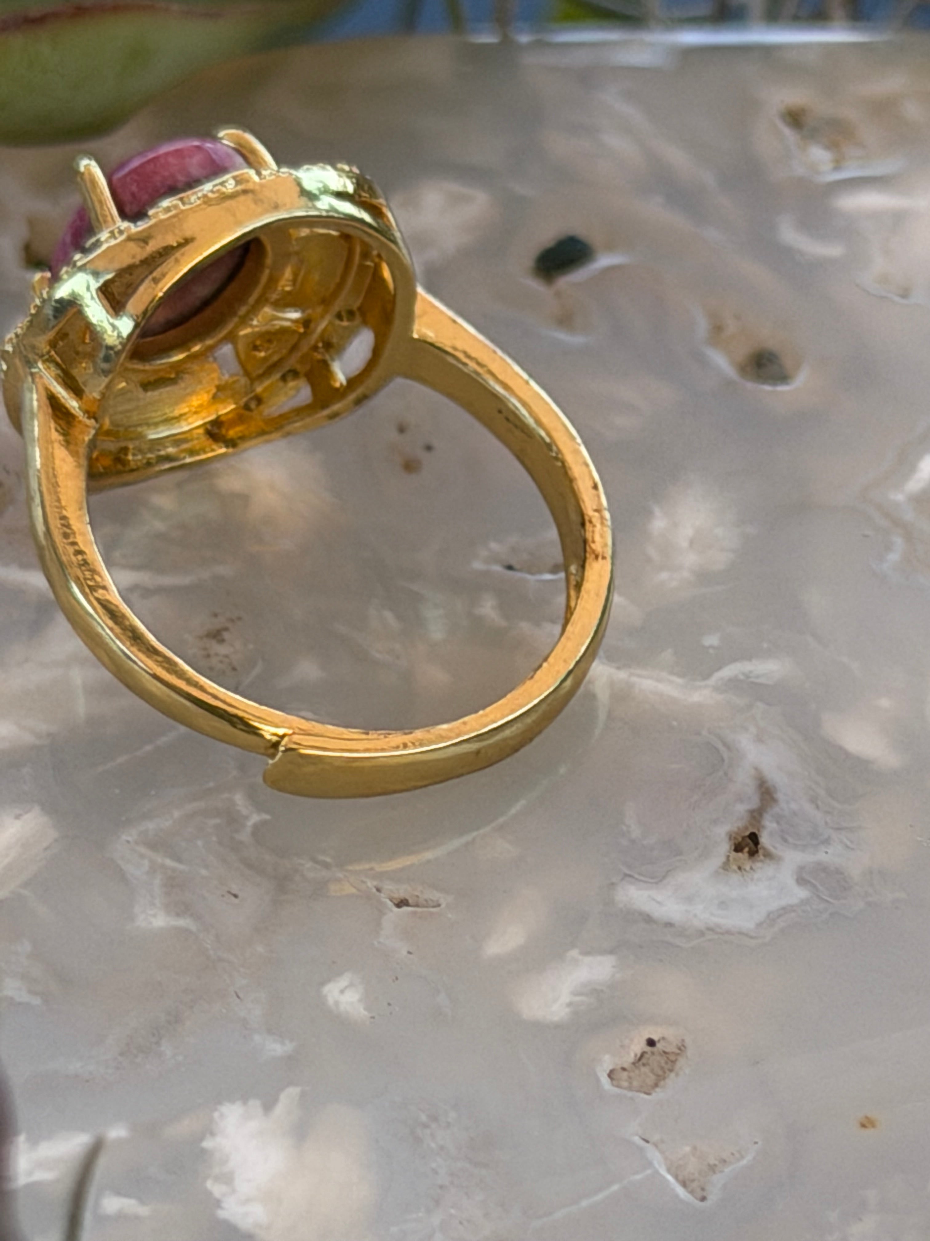 A gold ring with a large oval pink gemstone, shown close-up on a textured, translucent white surface.