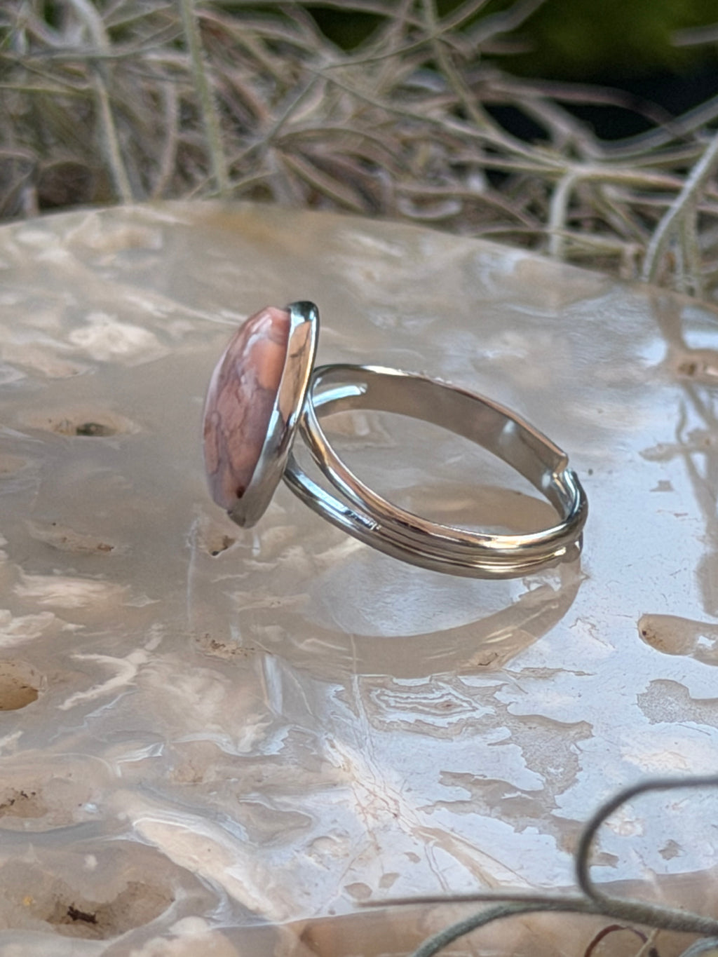 A silver-toned ring with a large, polished pinkish-red stone, displayed on a textured white glass surface.