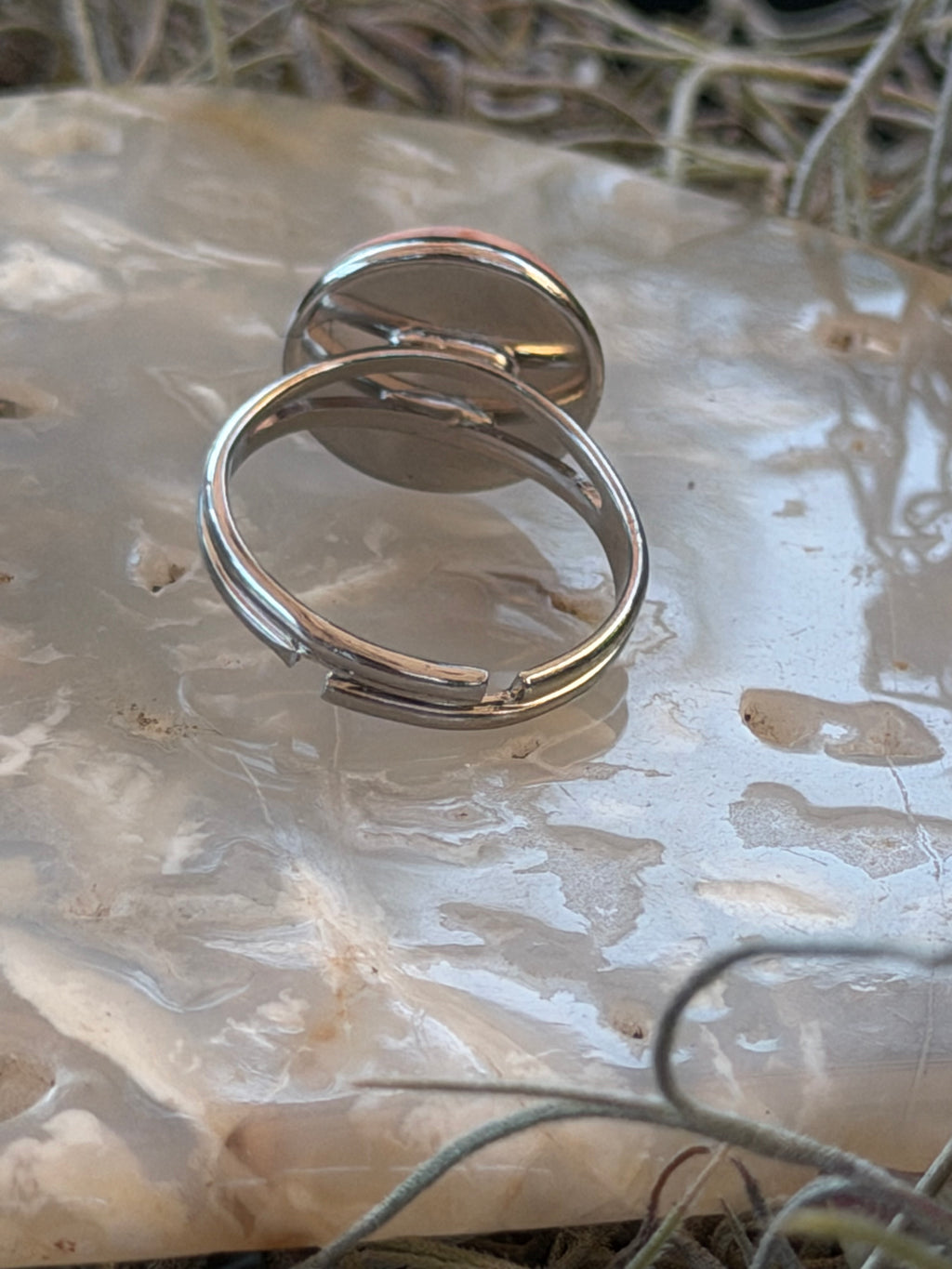 Two polished silver-toned metal hoop earrings resting on a smooth, translucent white stone surface with dried grass in the background.