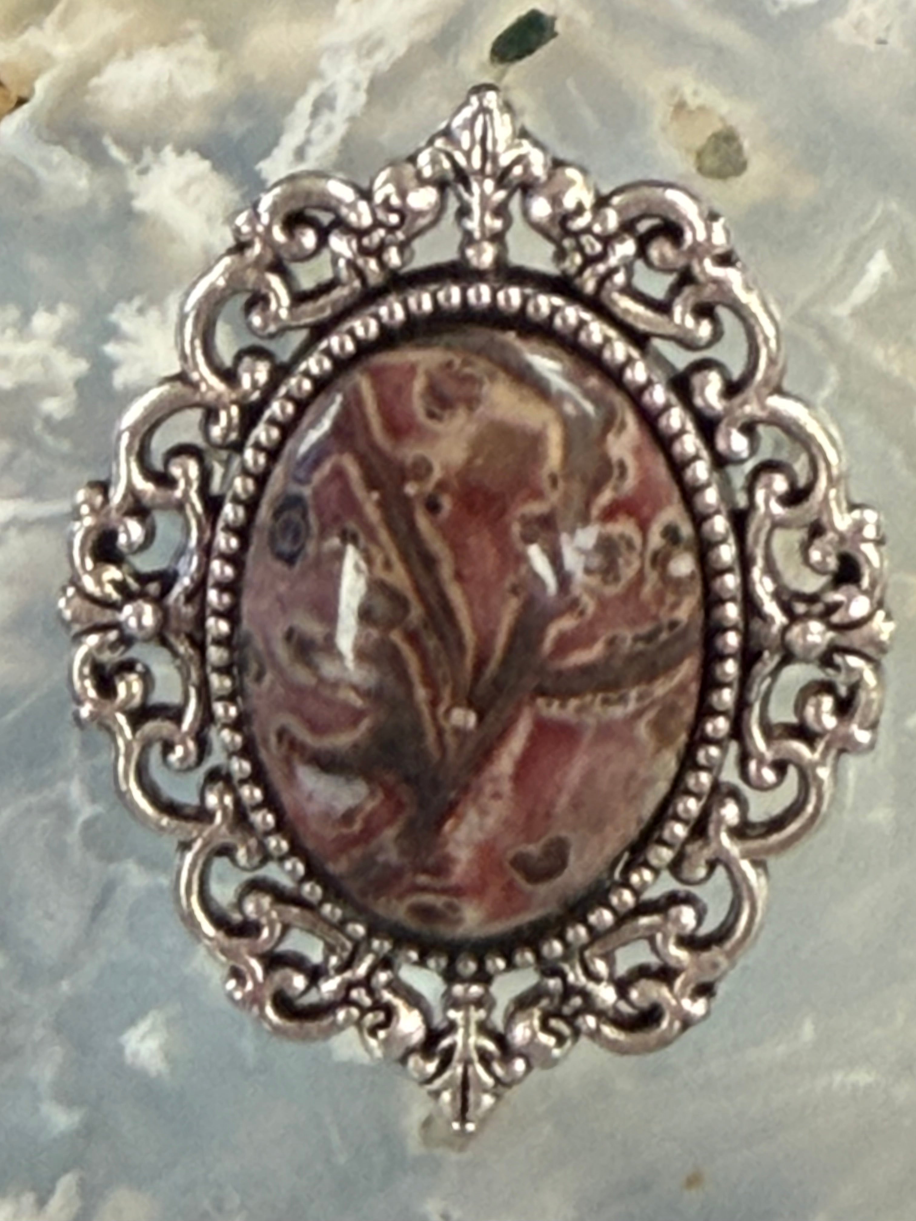 An ornate silver filigree Ring featuring a Oval Leopard Skin Jasper cabochon stone with a brown and beige marbled pattern, set against a textured gray background.